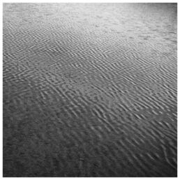 Close-up of rippled sand patterns on a beach in black and white