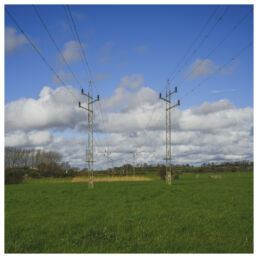 Two powerline towers standing in a green field under a blue sky with scattered clouds
